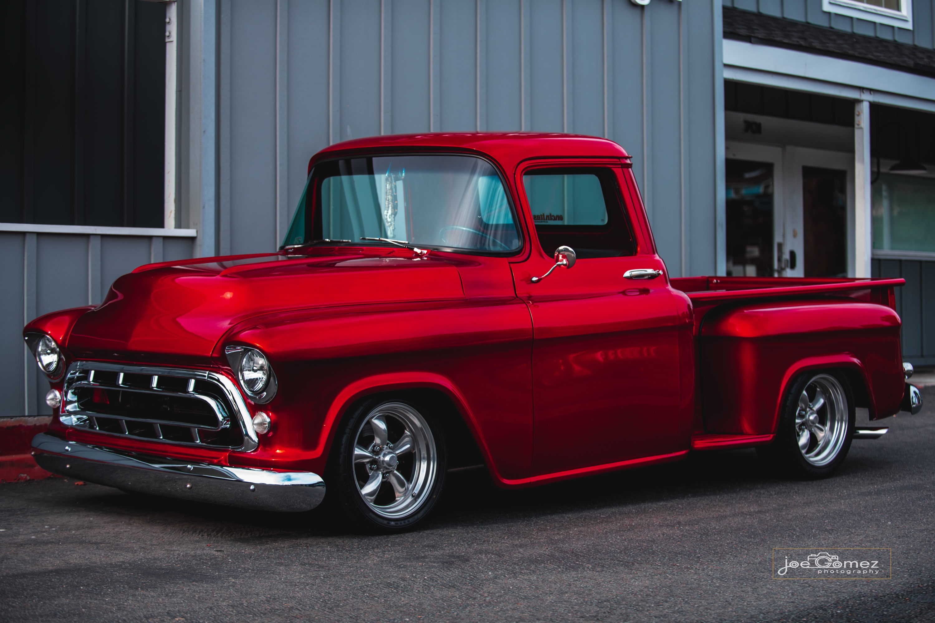 Red classic pickup in profile outside a coastal building