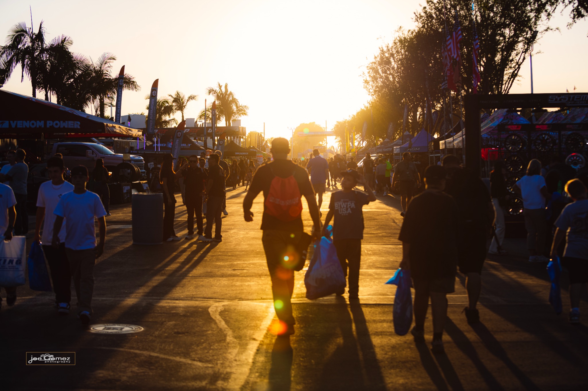 Visitors walking between show booths as the setting sun casts long shadows down the aisle