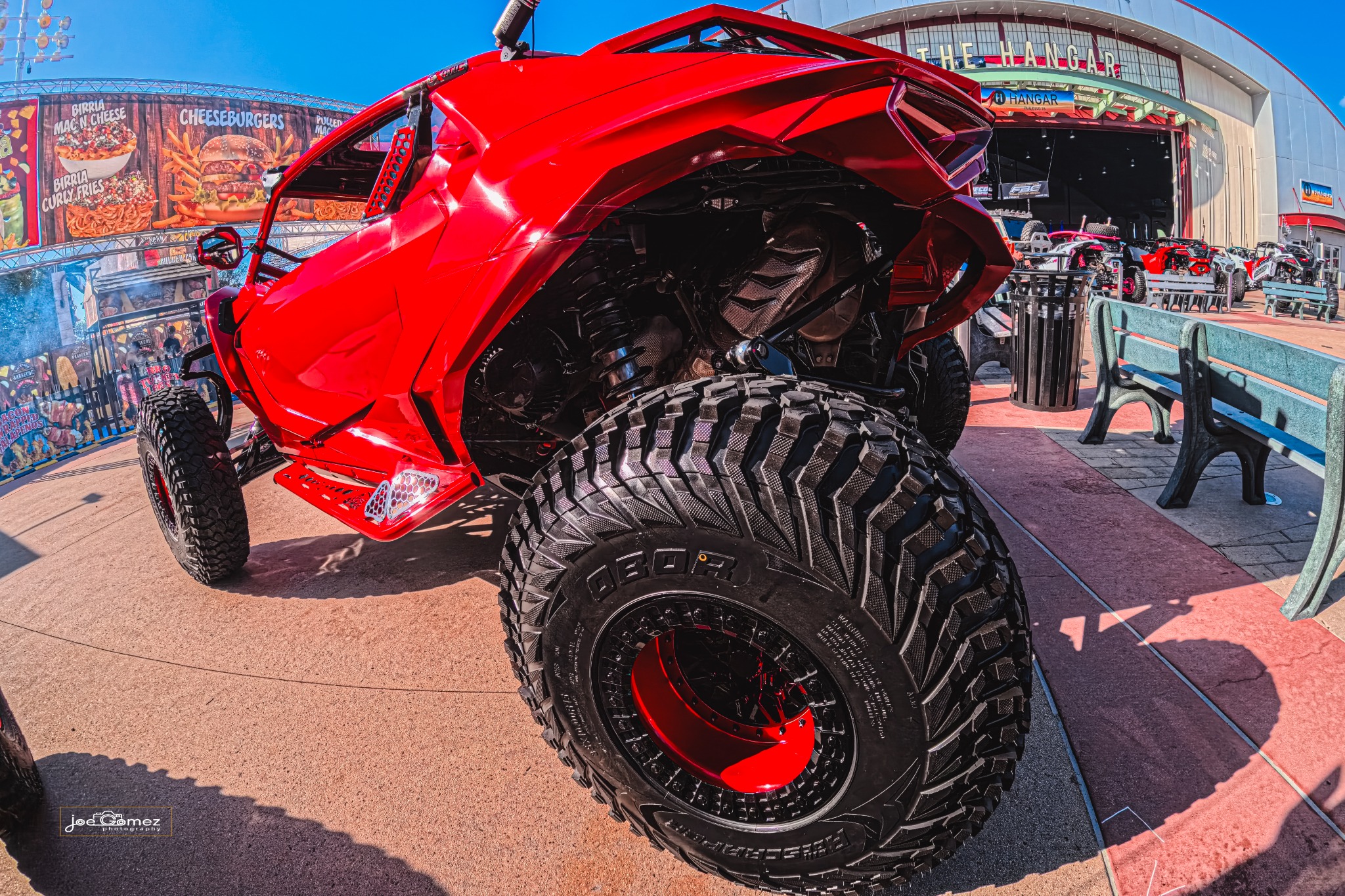 Rear-quarter view showing the red vehicle’s body contours and deep-tread tires