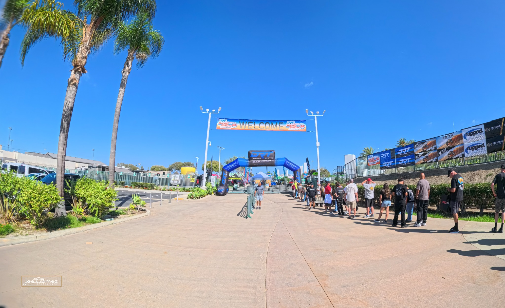 Visitors queue beside palm trees beneath the Sand Sports Super Show welcome banner and blue DRT arch