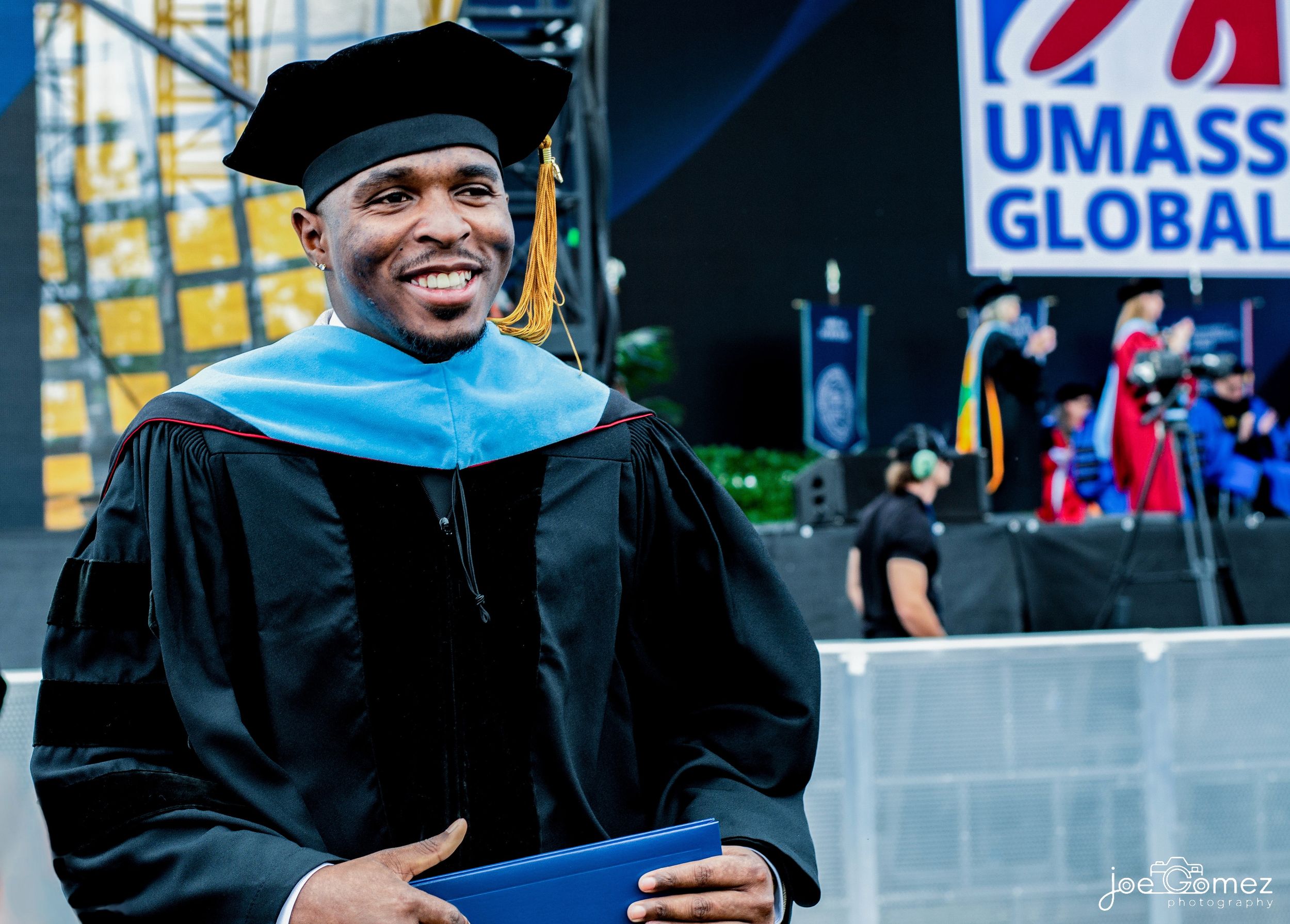 Doctorate graduate in academic regalia holding his diploma on the commencement stage in Southern California.